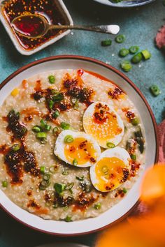 a bowl of oatmeal with boiled eggs on top and green onions next to it