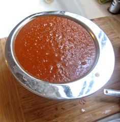 a metal pan filled with sauce on top of a wooden cutting board