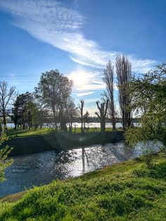 the sun shines brightly over a small river in an area with green grass and trees