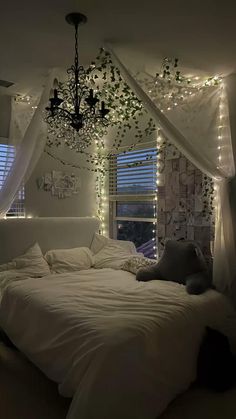 a bed with white sheets and lights hanging from the ceiling in front of a window