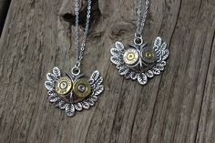 two silver and gold necklaces sitting on top of a piece of wooden plank with leaves