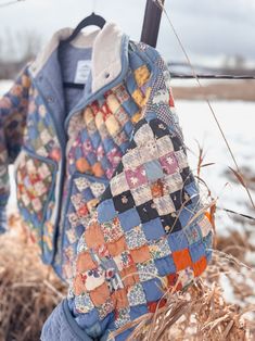 an old quilted jacket hanging on a fence post in the wintertime with snow