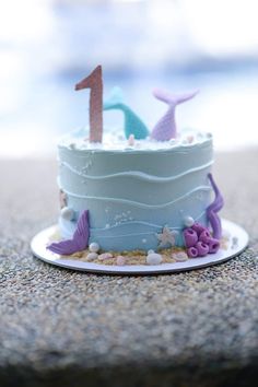 there is a blue cake with purple and white decorations on the top that has a number one on it