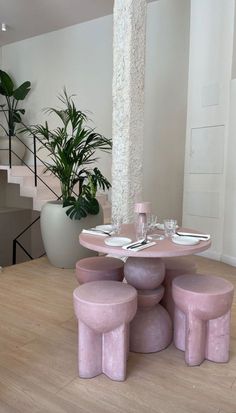 a pink table with four stools in front of it and a potted plant on the other side