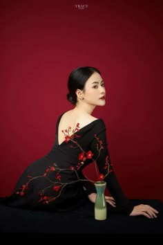 a woman sitting on the ground with a vase in front of her and red background