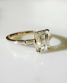 an engagement ring with a green diamond and two baguettes on the side, sitting on a white surface