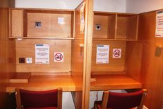 two wooden desks with red chairs in front of them and signs on the wall behind them