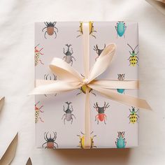 a gift wrapped in white paper with colorful bugs on it and ribbon tied around the top