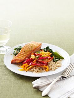 a white plate topped with fish and rice next to a glass of water on top of a table