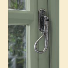 a metal hook on the side of a green door with a window in the background