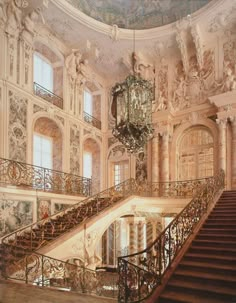 an ornate staircase with chandelier and paintings on the walls in a large building