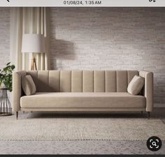 a beige couch sitting in front of a brick wall next to a lamp and rug