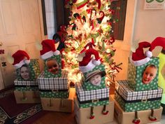 three children wearing christmas hats are sitting in boxes near a christmas tree with their faces on them