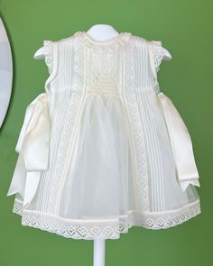 An elegant and delicate off-white dress with a geometrical smock detail and laces. It comes with a matching bonnet, and the dress has buttons on the back for closure. Made in Spain Dry clean Final sale, no exchanges nor returns are accepted Sleeveless Lace Dress With Smocked Back, Elegant Beige Dress With Smocked Bodice, Off White Lace Dress With Ruffles, White Baptism Dress For Spring Garden Party, Classic Daywear Dress With Smocked Bodice, Sleeveless Broderie Anglaise Dress For Garden Party, Sleeveless White Lace Baptism Dress, Sleeveless Dress With Smocked Back For Wedding, Elegant Summer Baptism Dress For Garden Party