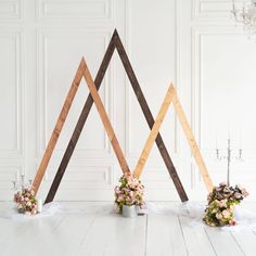 three wooden triangles on the floor with flowers in vases next to them and one is made out of wood