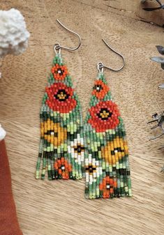 a pair of beaded earrings sitting on top of a wooden table next to flowers