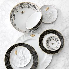 black and white plates with gold trim on them sitting on a marble countertop next to each other