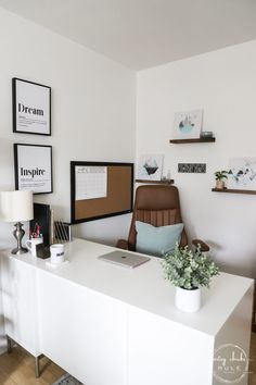 a white desk with a laptop on it and some pictures hanging above the desk in front of it