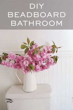 a white vase filled with pink flowers sitting on top of a toilet