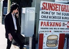 a man walking down the street while talking on a cell phone next to a sign that says sunset grill