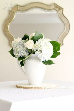 a white vase filled with flowers sitting on top of a table next to a mirror