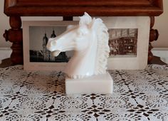 a white horse head sitting on top of a table next to a framed photo and an ornate wooden frame