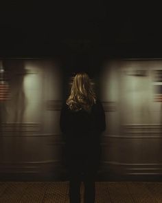 a woman standing in front of a train with her back to the camera and looking at it