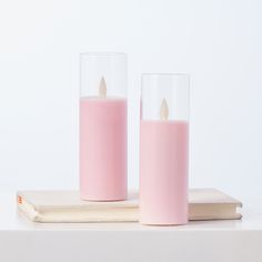 two pink candles sitting next to each other on top of a wooden book and white background