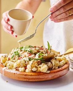 a person is pouring something into a bowl with food on the table next to them