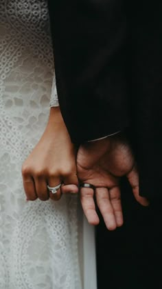 a close up of two people holding hands with rings on their fingers and wearing wedding bands