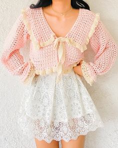 a woman wearing a pink top and white lace skirt standing in front of a wall