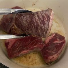 two pieces of meat in a bowl with tongs