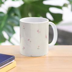 a white coffee mug sitting on top of a wooden table next to a book and plant