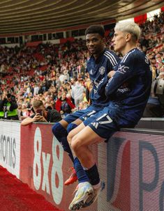 two soccer players are sitting on a wall in front of an audience at a game