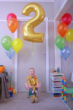 a baby sitting on a tricycle with balloons in the shape of numbers 2 and 3