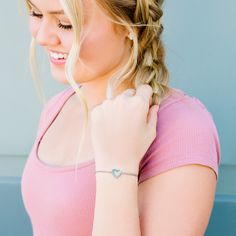 a woman with blonde hair wearing a pink shirt and a heart shaped bracelet on her wrist