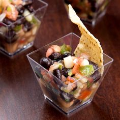 three small plastic cups filled with food on top of a wooden table next to a tortilla chip