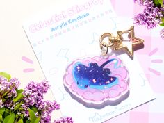 a pink and blue heart shaped keychain sitting on top of a table next to purple flowers