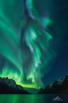 an aurora bore is seen in the night sky over mountains and water with green lights