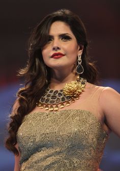 a woman with long hair wearing a gold and silver dress, necklace and earring