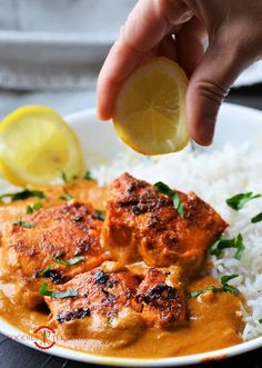 someone is holding a lemon over some food on a plate with rice and gravy