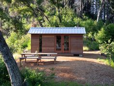 a small cabin in the woods with a picnic table and bench next to it,