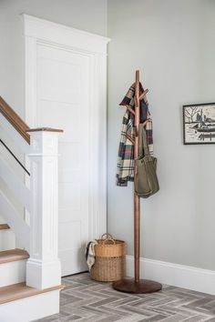 a coat rack with two coats hanging on it next to a basket and some stairs