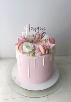 a pink birthday cake with white icing and macaroons