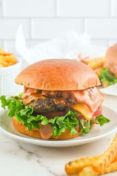 a hamburger with meat, lettuce and cheese on a plate next to french fries