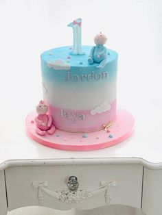 a baby's first birthday cake on top of a white table with pink and blue frosting