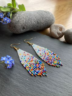 two pairs of beaded earrings sitting on top of a table next to rocks and flowers