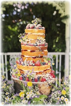 a multi layer cake sitting on top of a table covered in flowers and strawberries