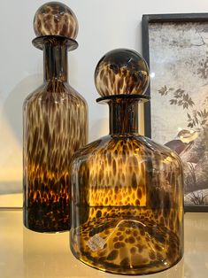 two glass vases sitting next to each other on a table with pictures behind them