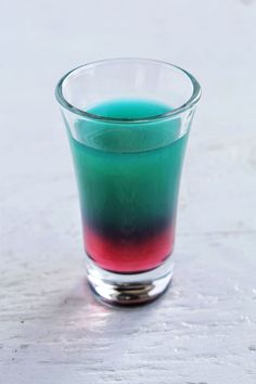 a glass filled with liquid sitting on top of a white table next to a red and green substance